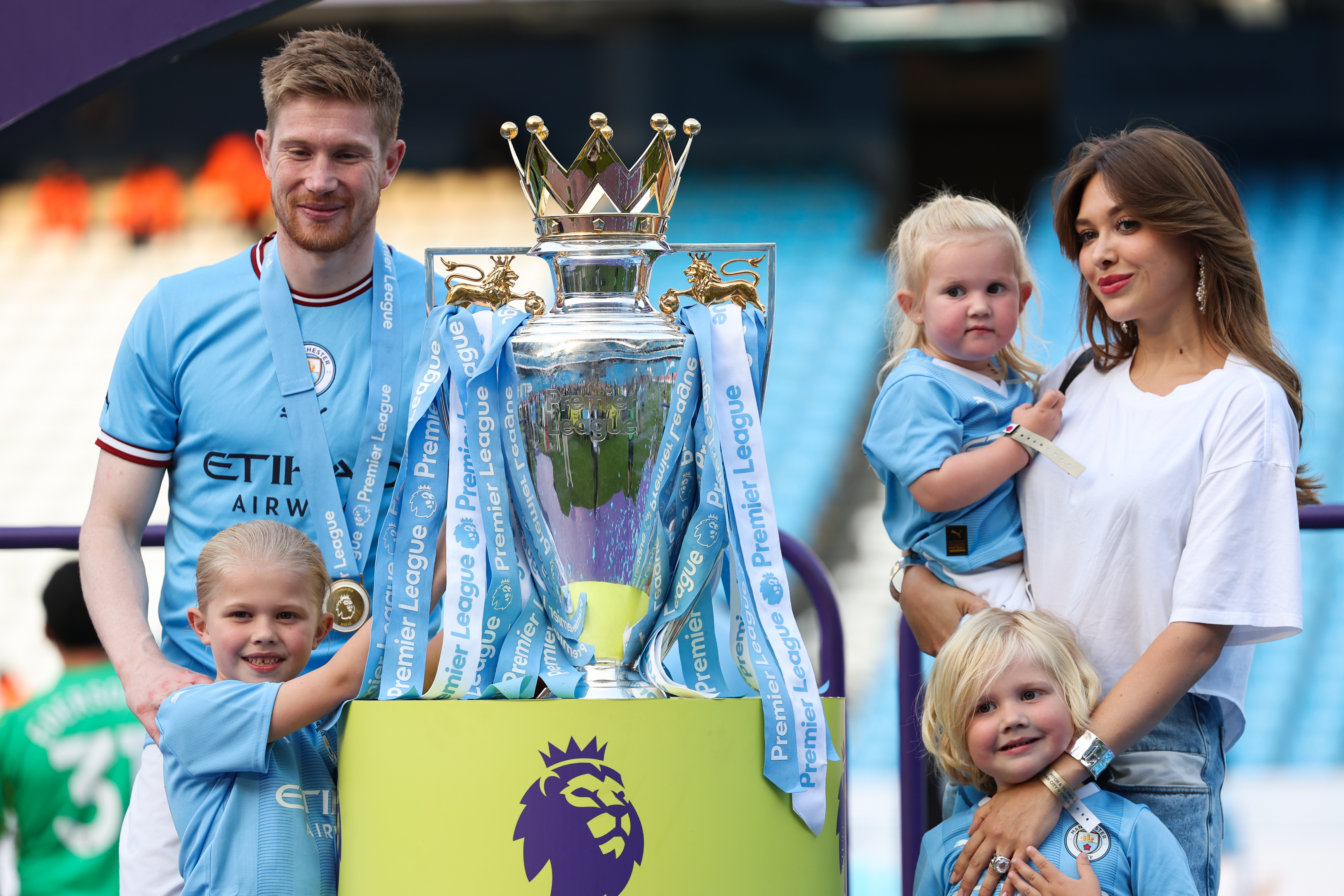 Kevin De Bruyne and Michelle Lacroix pose next to the Premier League trophy with their brood